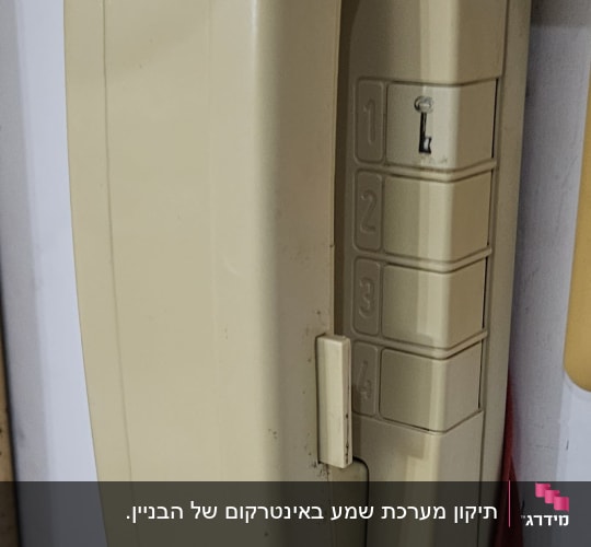 אינטרקום ישן עם מדבקה ירוקה על הקיר